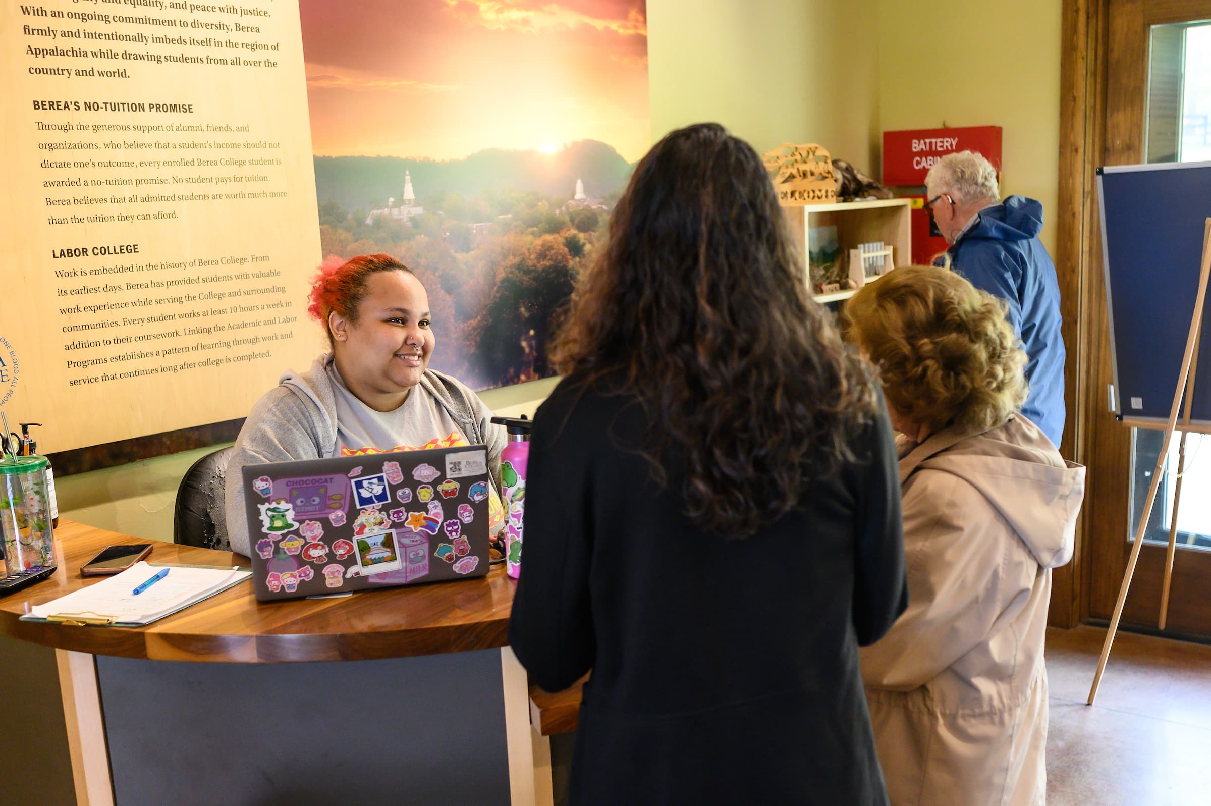 A student assisting visitors at a desk with their laptop.