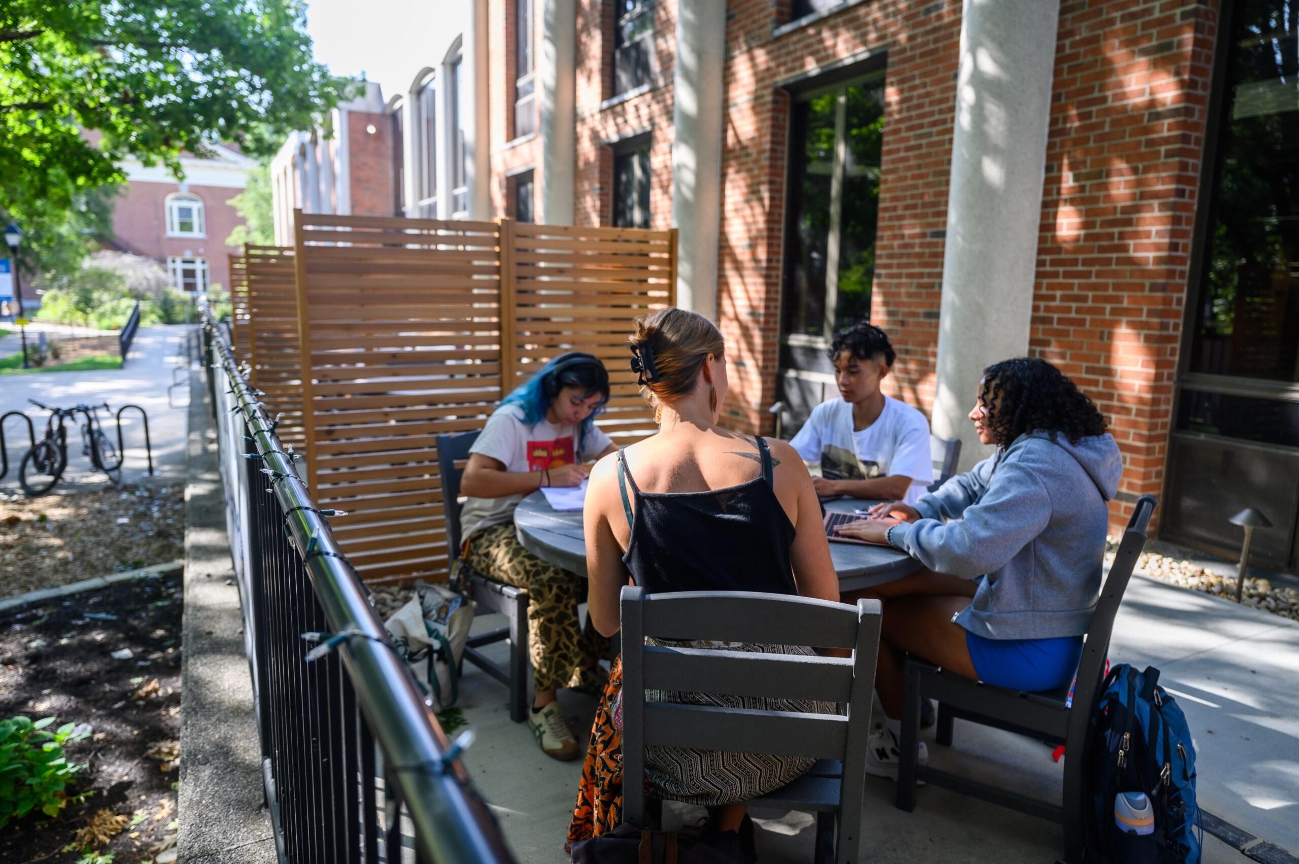 Several students are sitting at an outdoor table, engaged in studying.