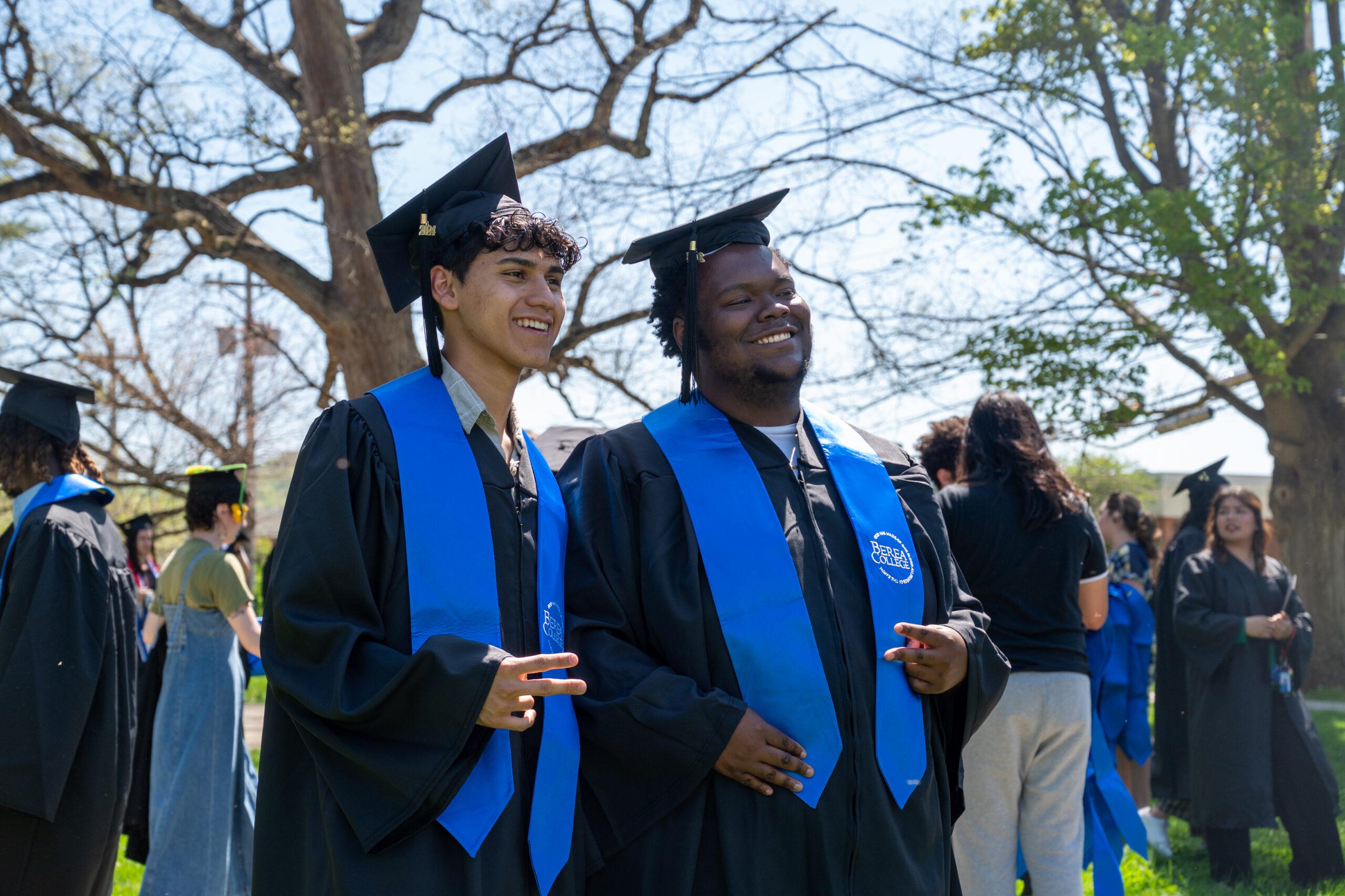 Two students at graduation in their caps and gowns posing for the camera.