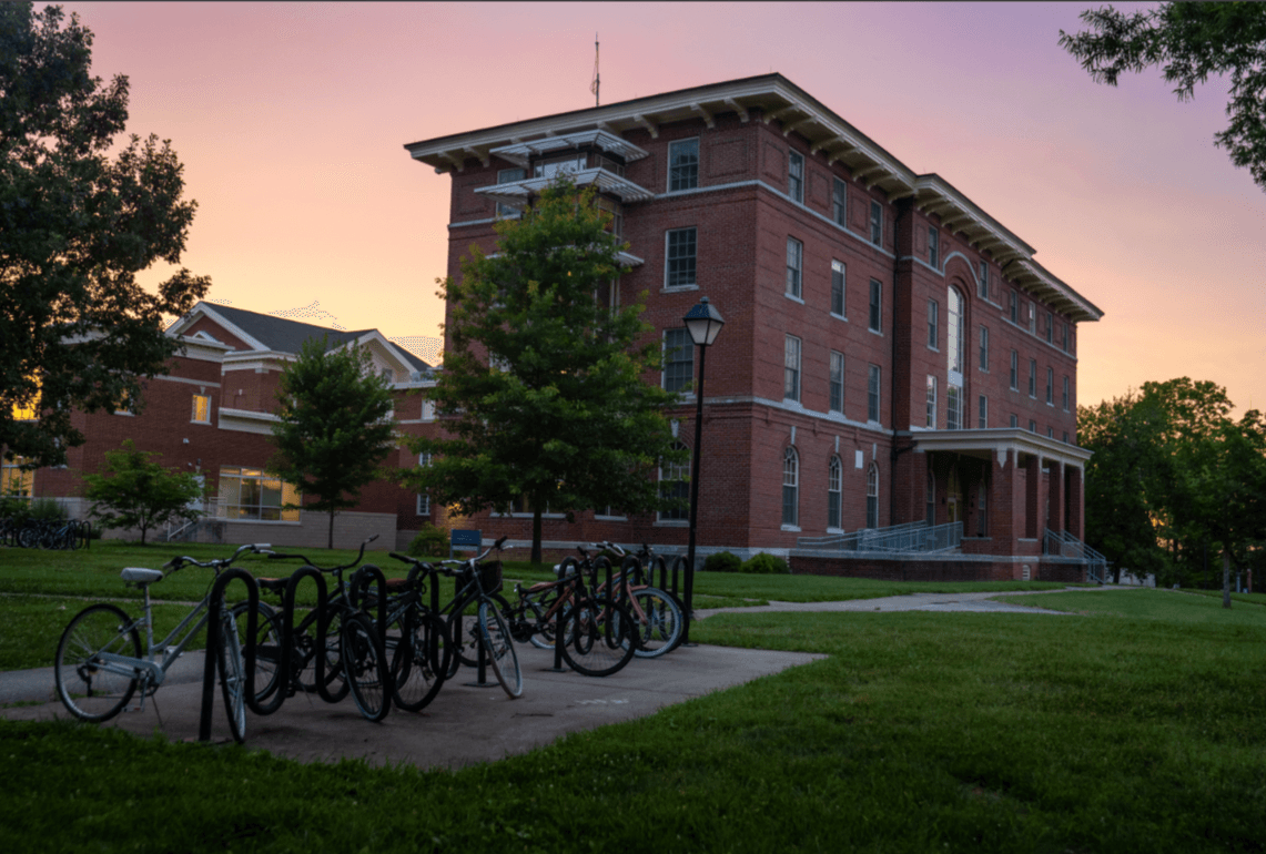 Photo of a sunset on Berea's campus featuring a dorm building and a bike rack.